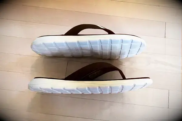 Adidas Comfort Flip-Flops on a wood floor with soles visible