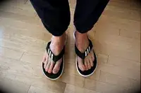 Feet wearing Adidas Comfort Flip Flops on wood floor