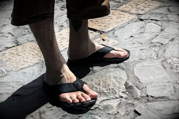 A person wears the Reef The Deckhand sandals while walking on stone