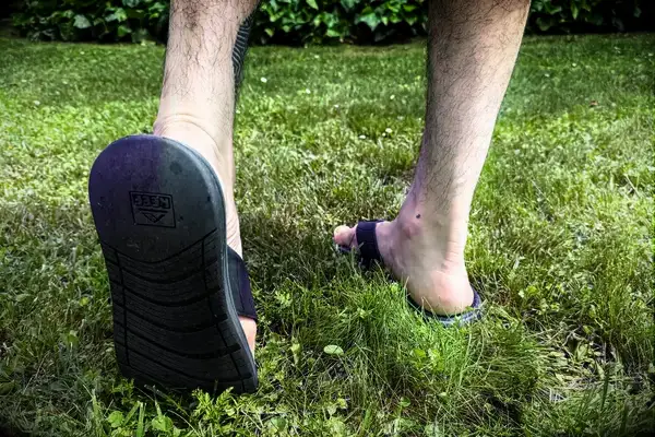 A person walks through grass while wearing the Reef The Deckhand sandals