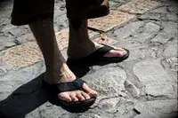 A person wears the Reef The Deckhand sandals while walking on stone