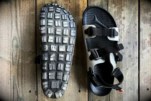 Quoc x Restrap Sandals shown on a wooden surface one displaying the tread pattern of the sole and the other showing the straps and upper design