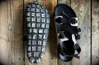 Quoc x Restrap Sandals shown on a wooden surface one displaying the tread pattern of the sole and the other showing the straps and upper design