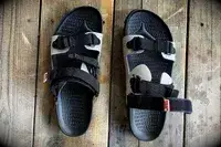 Quoc x Restrap Sandals with adjustable black straps on a wooden surface