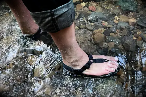 A person stands in a stream wearing Bedrock Cairn Adventure Sandals