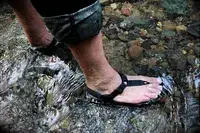 A person stands in a stream wearing Bedrock Cairn Adventure Sandals