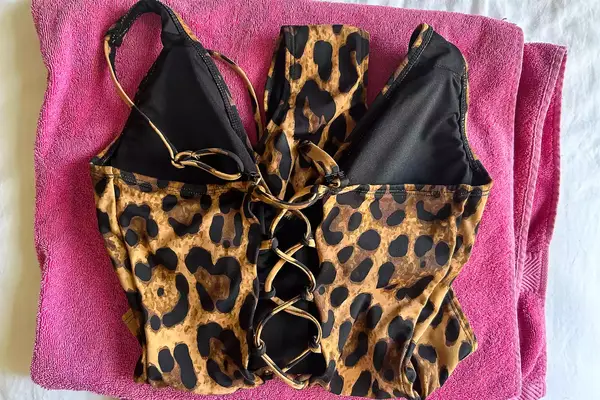 A TA3 Brazilian Plungey Swimsuit with laced details placed on a pink towel