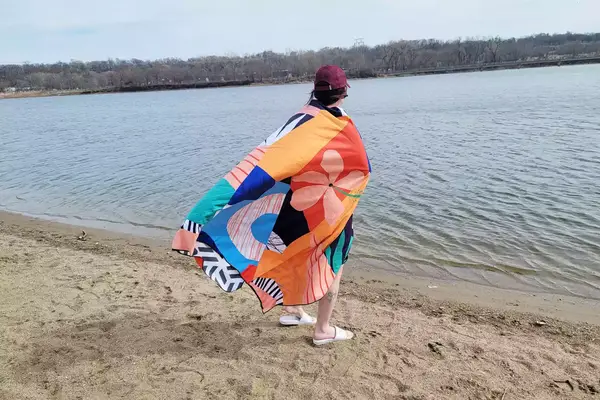 Person wrapped in the Ocoopa Diveblues Microfiber Beach Towel while standing on sand by the water