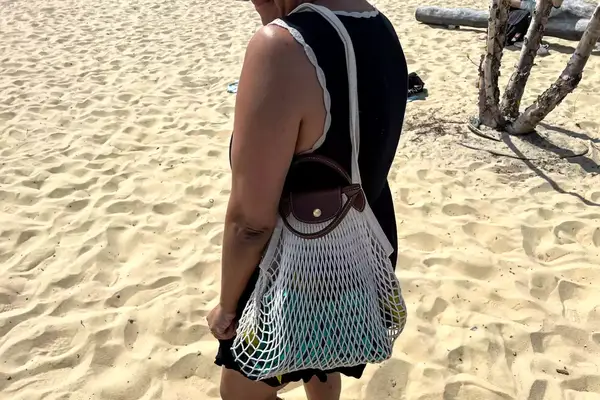 A person carries the Longchamp Le Pliage Filet L Mesh Bag using the shoulder strap