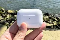 Hand holding Apple AirPods Pro 2 case near a rocky shoreline