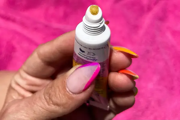 A hand with manicured nails holding Lanolips Sun Balm SPF 30 with its cap off, showing a yellow substance on the nozzle