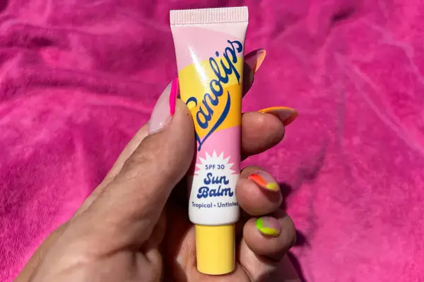 A hand holding a Lanolips SPF 30 Sun Balm against a pink background