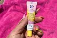 A tube of Lanolips Sun Balm SPF 30 held in a hand with colorful nails, a pink towel in the background