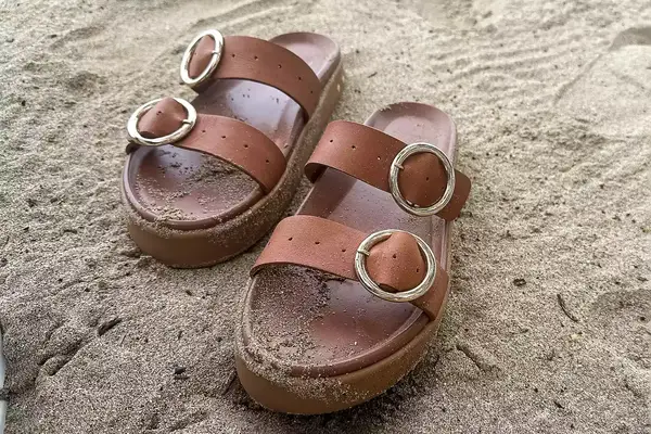 Beek Warbler Leather Platform Platform Leather Slides covered in sand with a sand background