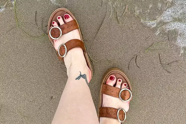 A person wearing the Beek Warbler Leather Platform Platform Leather Slides in the sand