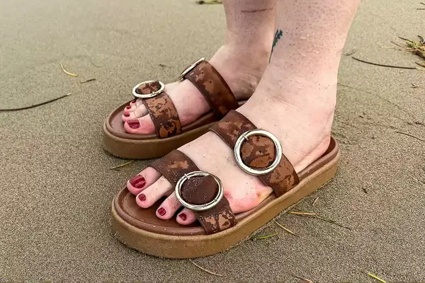 A person wearing the Beek Warbler Leather Platform Platform Leather Slides on the sand