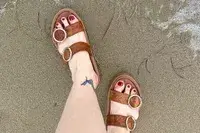 A person wearing the Beek Warbler Leather Platform Platform Leather Slides in the sand