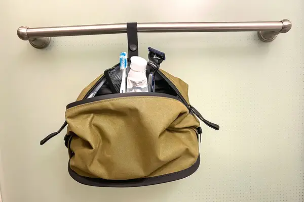 A hand unzipping a Bagsmart Toiletry Bag for Men on a testing cart with mini travel sized items