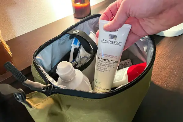 A hand putting travel sized conditioner inside of a Bagsmart Toiletry Bag for Men