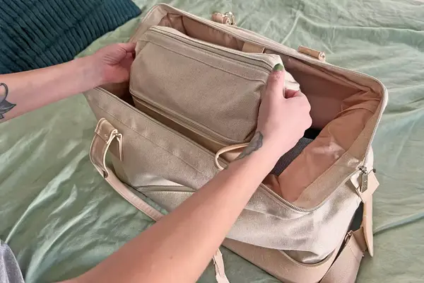  Away Large Toiletry Bag on a dresser with cologne, a mini bottle of shampoo, razor, and lotion around it