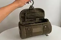 A person holds the Dagne Dover Small Seoul Dopp Kit by the hook