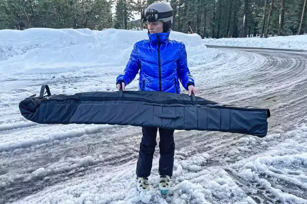 A person carries the DB Snow Roller Pro 127L by the top handles