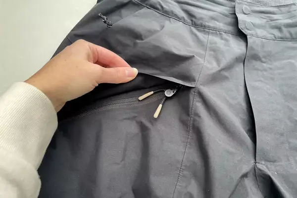 A person lifts the flap on the zippered pocket on the Backcountry CrestCarver Men