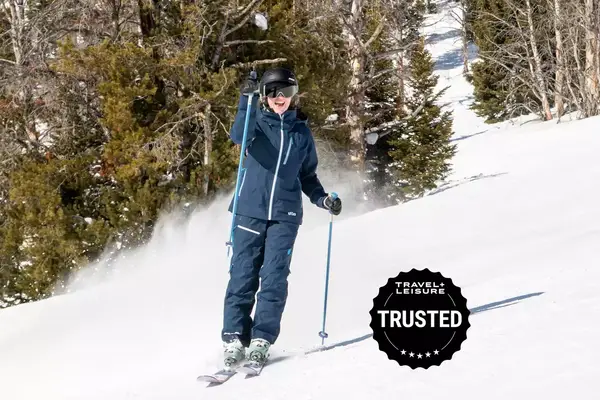 person skiing on a ski run raising hand smiling