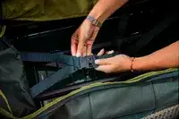 A person adjusts the straps on the Away The Outdoor Rolling Duffel 85L