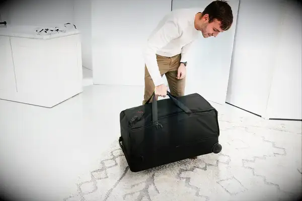 Person lifting Tumi Alpha 3 Large Split 2-Wheeled Duffel up off a white and gray rug