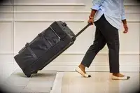 Person lifting Tumi Alpha 3 Large Split 2-Wheeled Duffel up off a white and gray rug