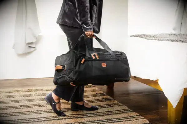 Gonex Rolling Duffel Bag With Wheels displayed upright in front of floral wallpaper