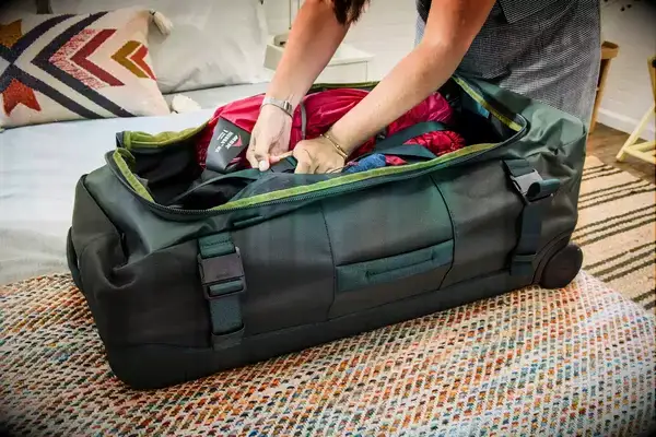 A person places clothing into the Away The Outdoor Rolling Duffel 85L