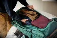 A person packing clothes into the REI Co-op Big Haul 34-inch Rolling Duffel