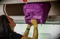 A person putting the Vera Bradley Adair Rolling Duffel Bag into an overhead bin