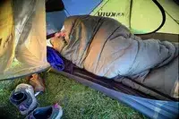 A person sleeps in a sleeping bag inside the Kuiu Mountain Star 2 Person Tent