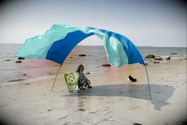 Person sitting under a windpowered canopy on a sandy beach with the sea in the background