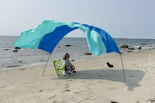 Person sitting under a windpowered canopy on a sandy beach with the sea in the background