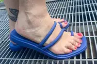 A woman wearing the Crocs Miami Toe Loop sandals on a metal grid surface, feet exposed with nail polish