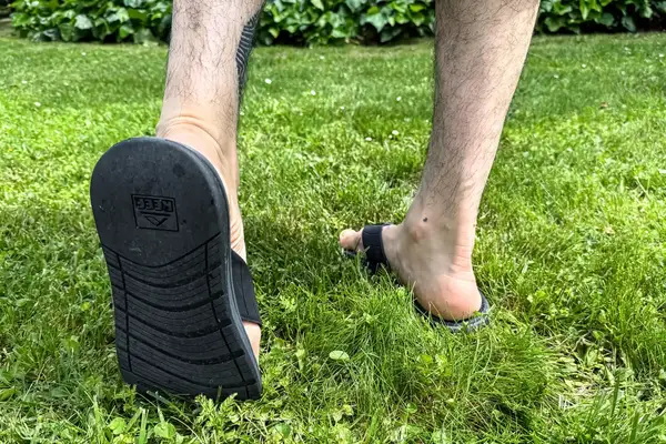 A person walks through grass while wearing the Reef The Deckhand sandals