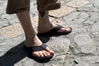 A person wears the Reef The Deckhand sandals while walking on stone
