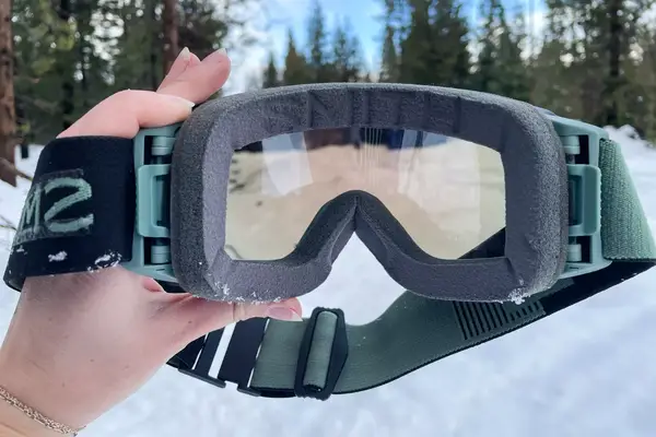 A hand holding the Smith I/O Mag Goggles in the snow