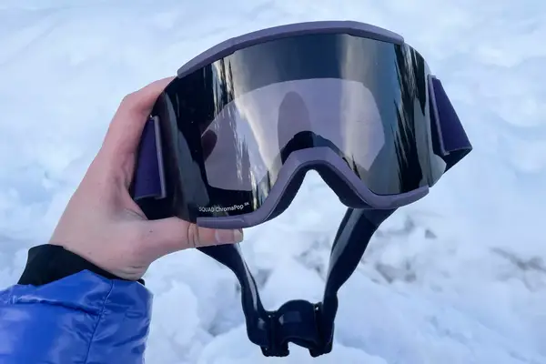 A person holding the Smith Squad Goggles over the snow