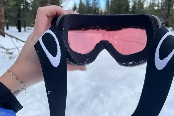 A person holding the Oakley Line Miner Pro L Snow Goggles outside in the snow