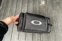 A person holding the carry bag for the Oakley Line Miner Pro L Snow Goggles
