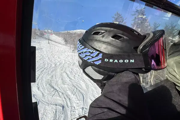 A person holding a helmet and Dragon NFX Mag OTG goggles on a ski lift