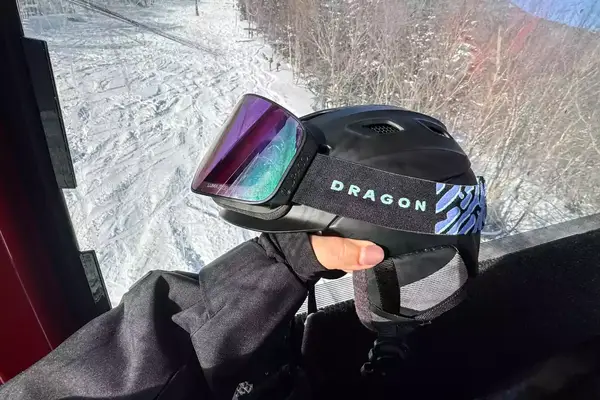 A person holding a helmet and the Dragon NFX Mag OTG goggles