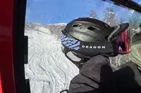 A person holding a helmet and Dragon NFX Mag OTG goggles on a ski lift