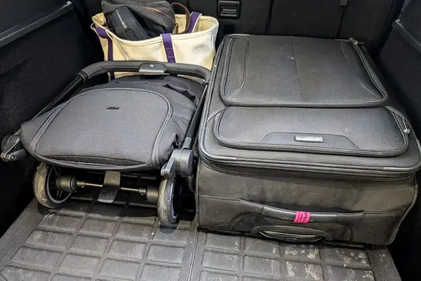 A folded Joolz Aer+ Lightweight Stroller, a suitcase and a tote bag placed in the trunk of a car