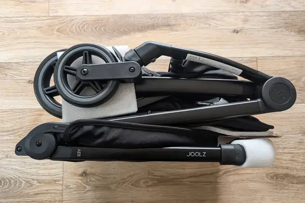 A folded Joolz Aer+ Lightweight Stroller resting on a wooden floor showing compact wheels and frame